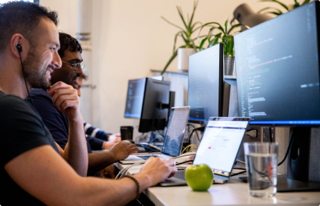 Smiling web development students sitting at workstations together, learning how to code at BrainStation Toronto.